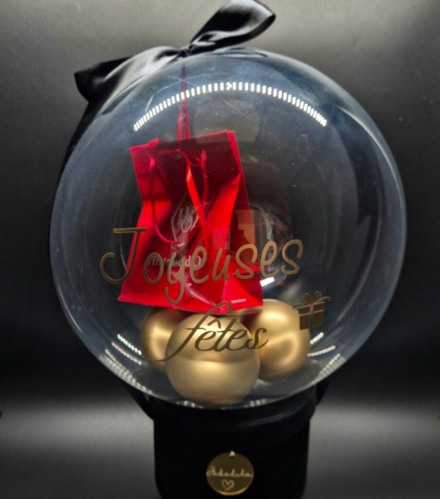 Boule de Noël transparente avec décor festif, ruban noir et ornements dorés dans un ballon bulle transparent avec un cadeau