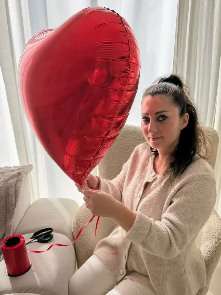 Jessica créatrice de Jakalila tient un grand ballon en forme de cœur rouge dans un salon lumineux.